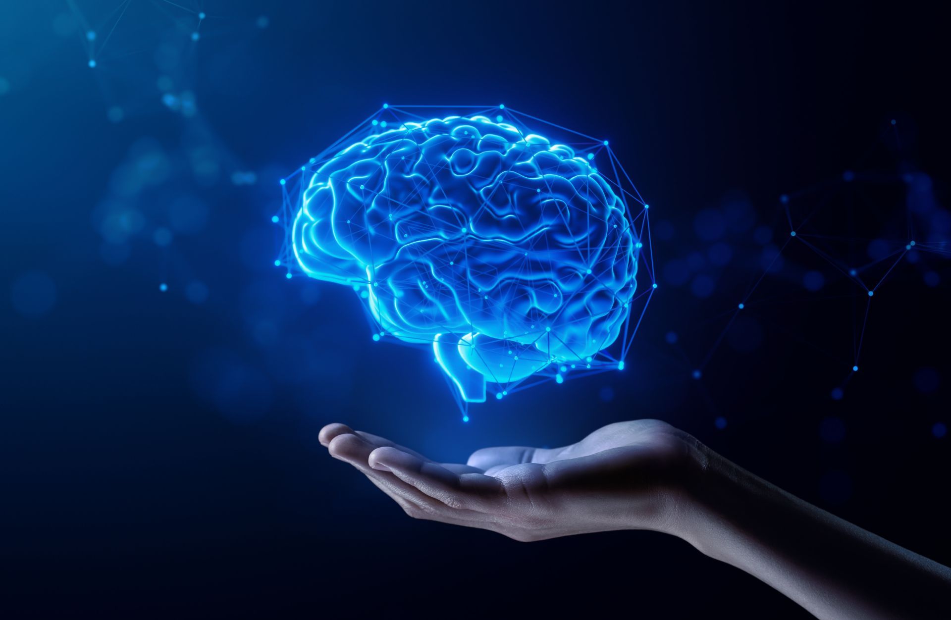 Glowing blue digital brain hovering above an outstretched hand on a dark background