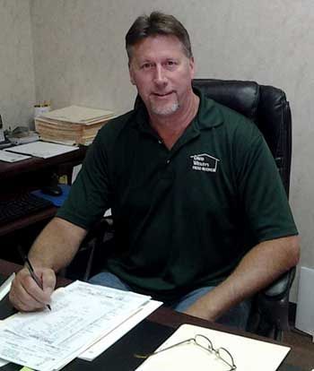Man in green shirt, seated at desk, writing on paperwork. Office setting with documents.