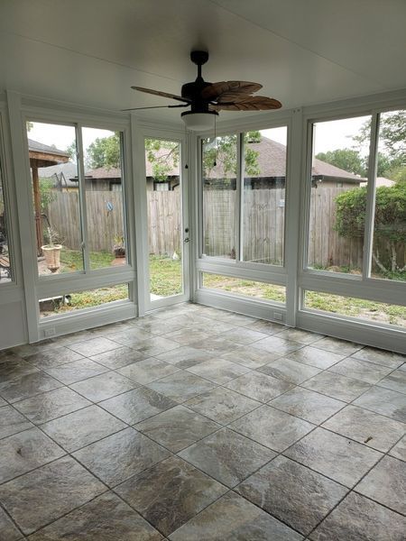 Sunroom with tiled floor, large windows, and a ceiling fan, overlooking a fenced backyard.