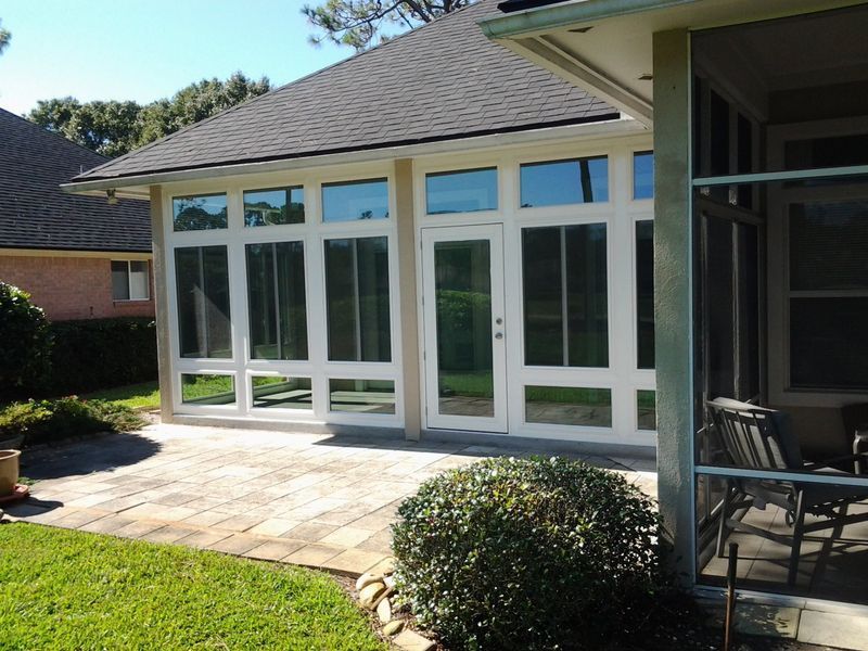 Screened-in patio extension of a house with dark roof and brick pavers; tan and white walls.
