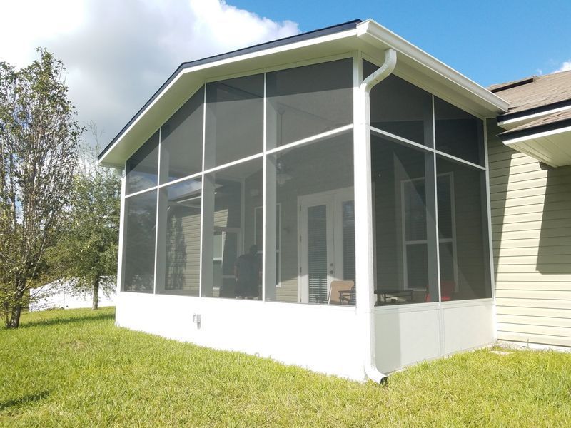 White screened-in patio attached to a light green house with white trim.