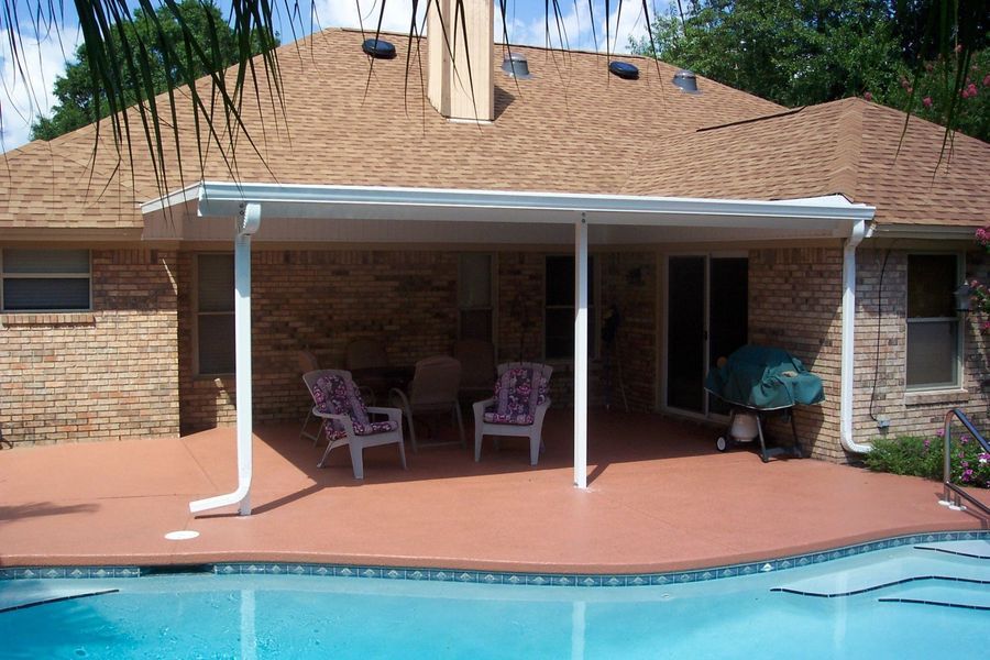 Patio with awning overlooking a pool. Chairs sit under the awning, next to a brick house.