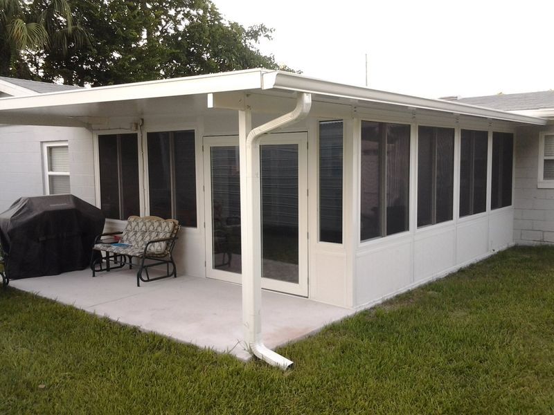 White screened-in patio attached to a house. Features concrete patio, grill, chairs, and glass doors. Green grass surrounds.