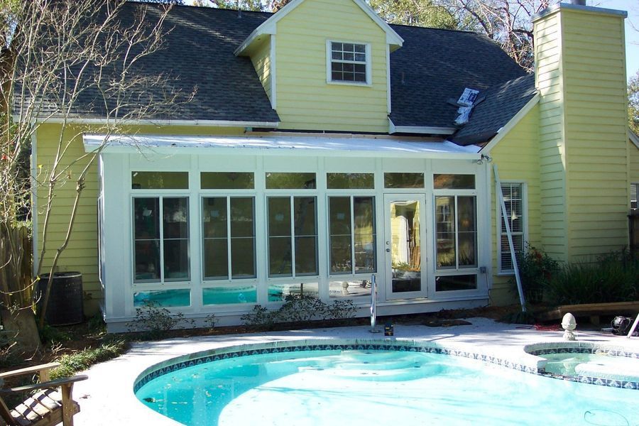 Yellow house with a white-framed sunroom overlooking a swimming pool.