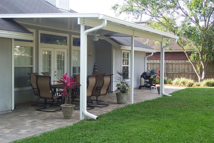 Covered patio with outdoor furniture, potted plants, and barbecue grill; home exterior.