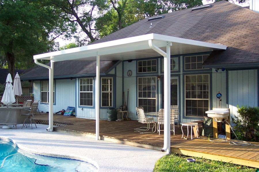 Patio cover over wooden deck next to a pool. White posts and roof; light blue house.
