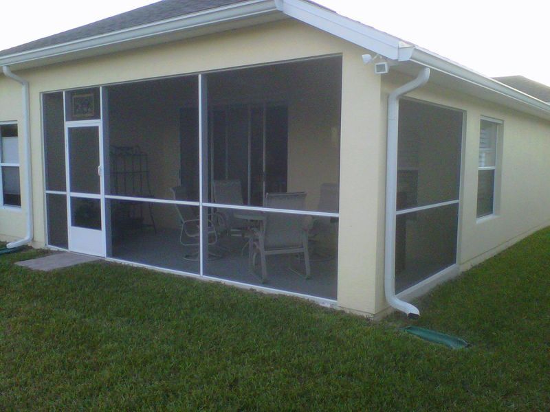 Screened-in porch on a beige house; white frames, door, and screens. Green lawn surrounds.