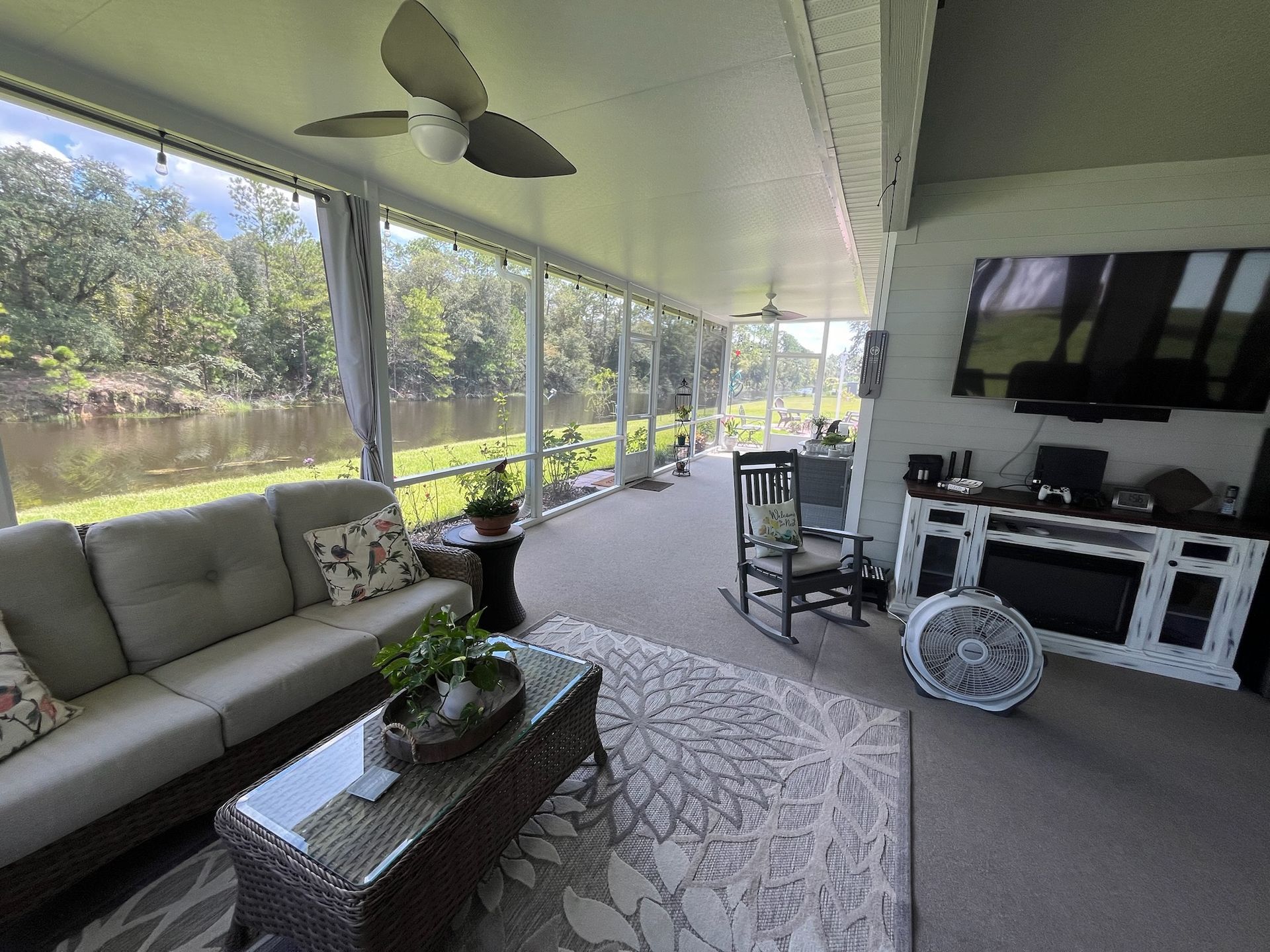 Screened porch overlooking a river, furnished with a sofa, TV, and fan.