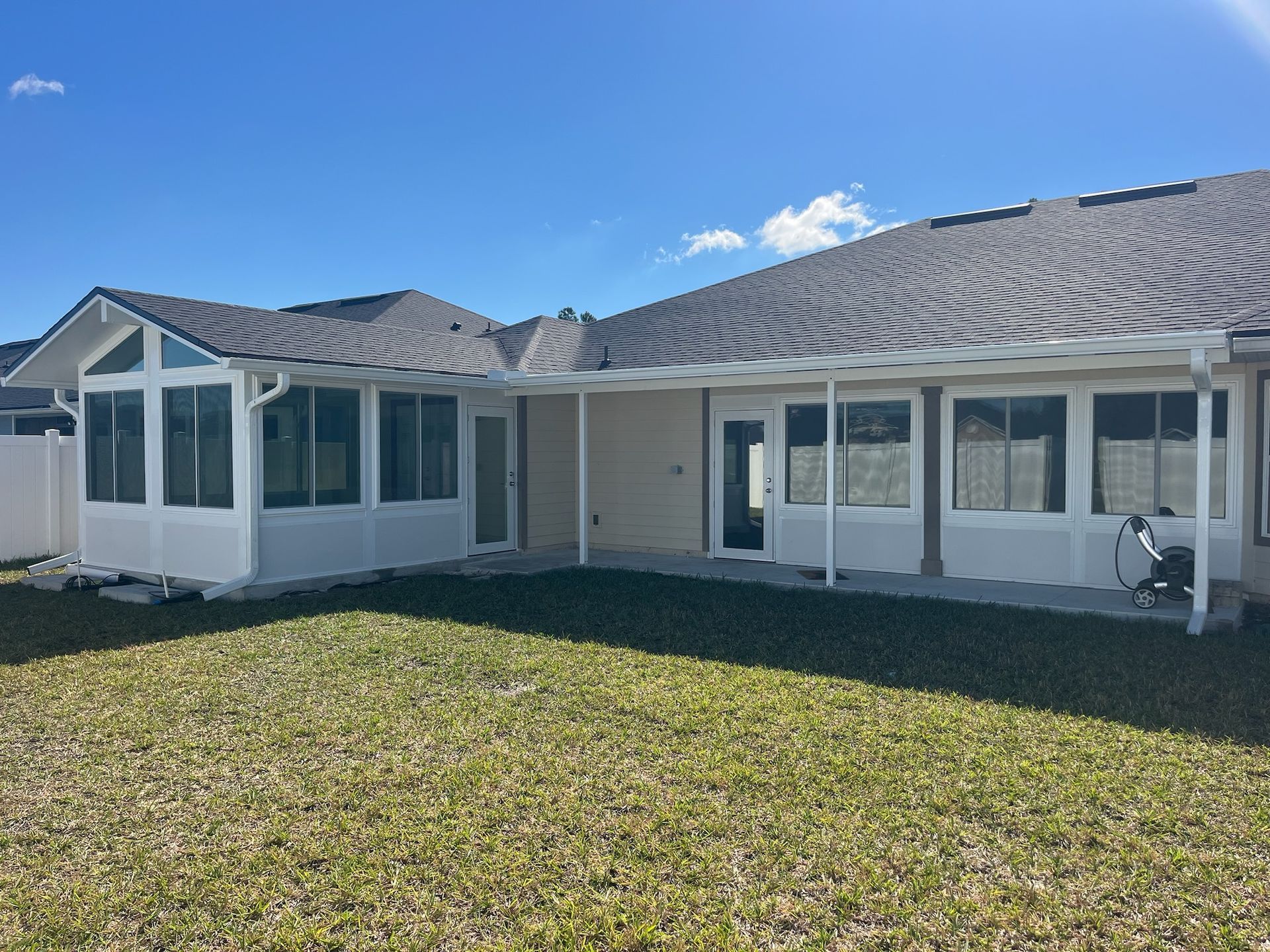 White sunroom attached to a house with a dark roof and a grassy yard under a blue sky.