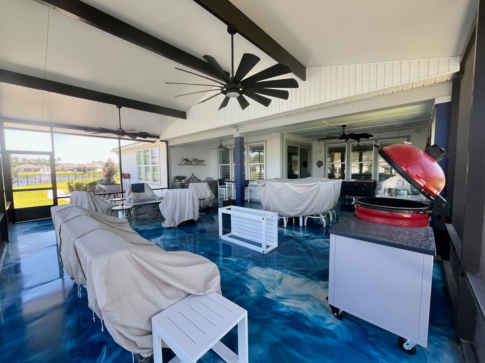 Spacious screened porch with blue epoxy floor, covered furniture, a grill, and a ceiling fan.