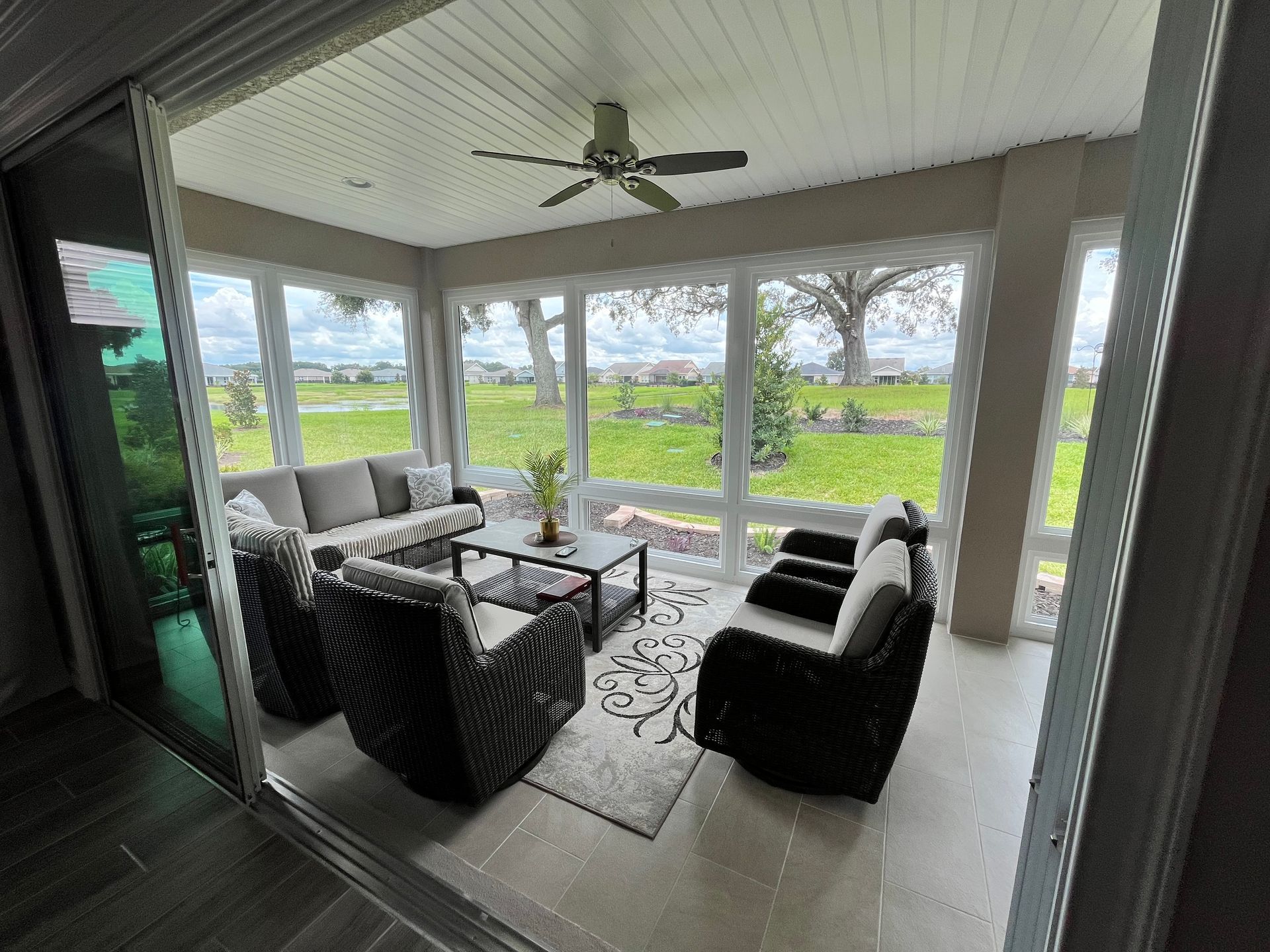 Sunroom with wicker furniture, glass windows overlooking a green lawn.
