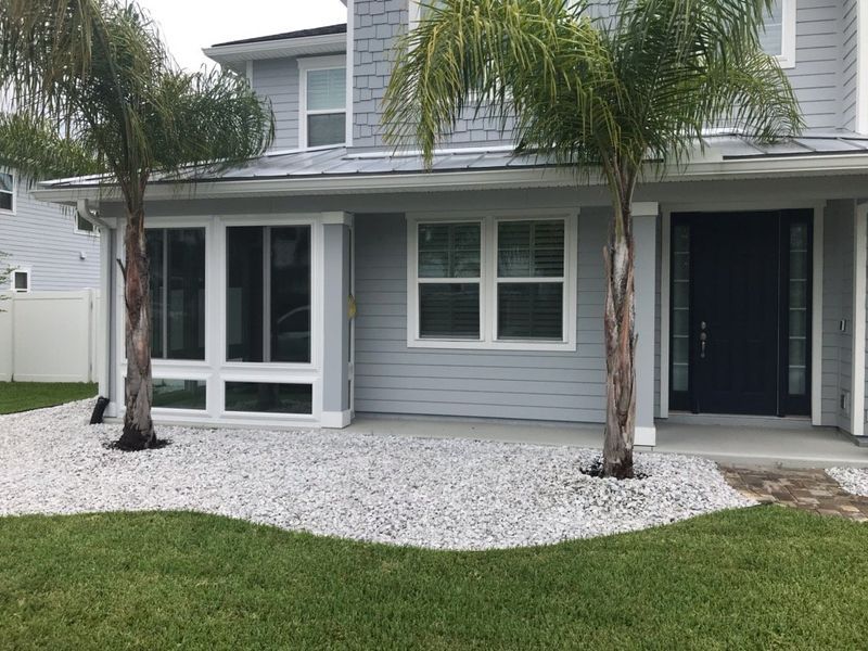 Light blue house with white trim, a dark door, and two palm trees in front. White gravel landscaping.