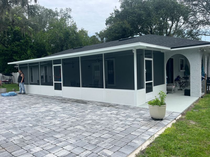 Screened-in patio with dark roof, white frame, gray pavers, and a person standing near it.