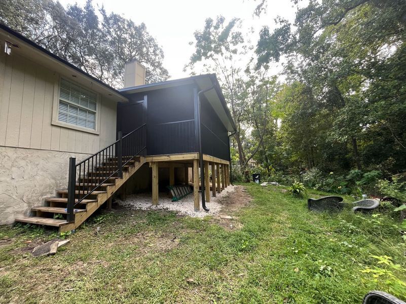 Backyard view of a house with a screened porch and wooden stairs leading down to a grassy yard.