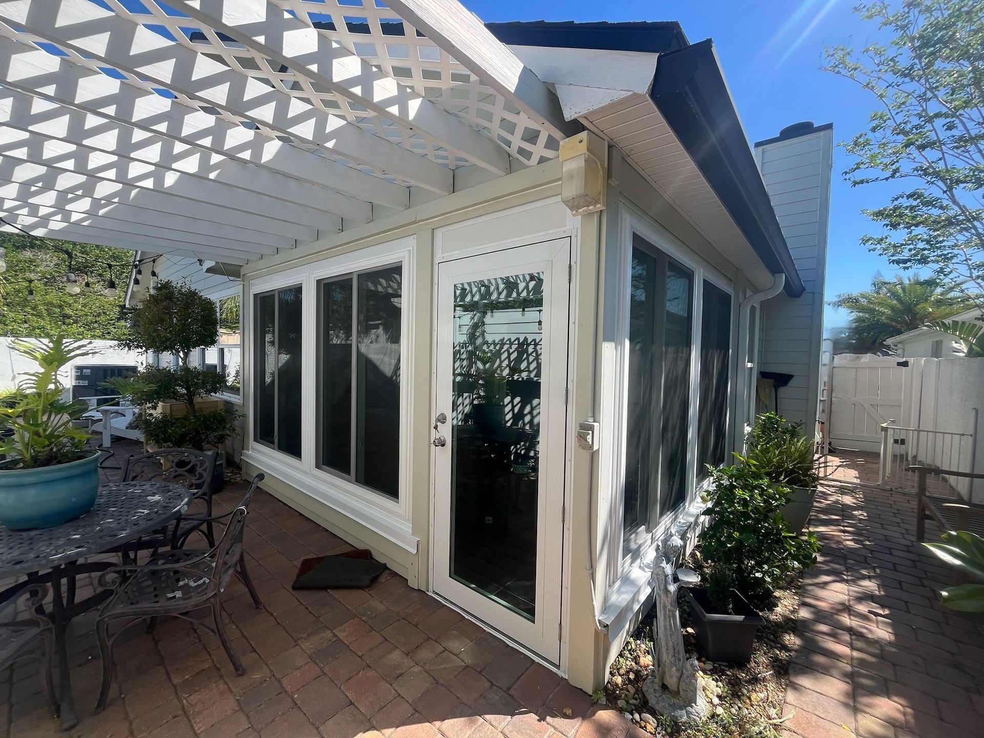 A sunroom with white trim and a latticed pergola on a brick patio.