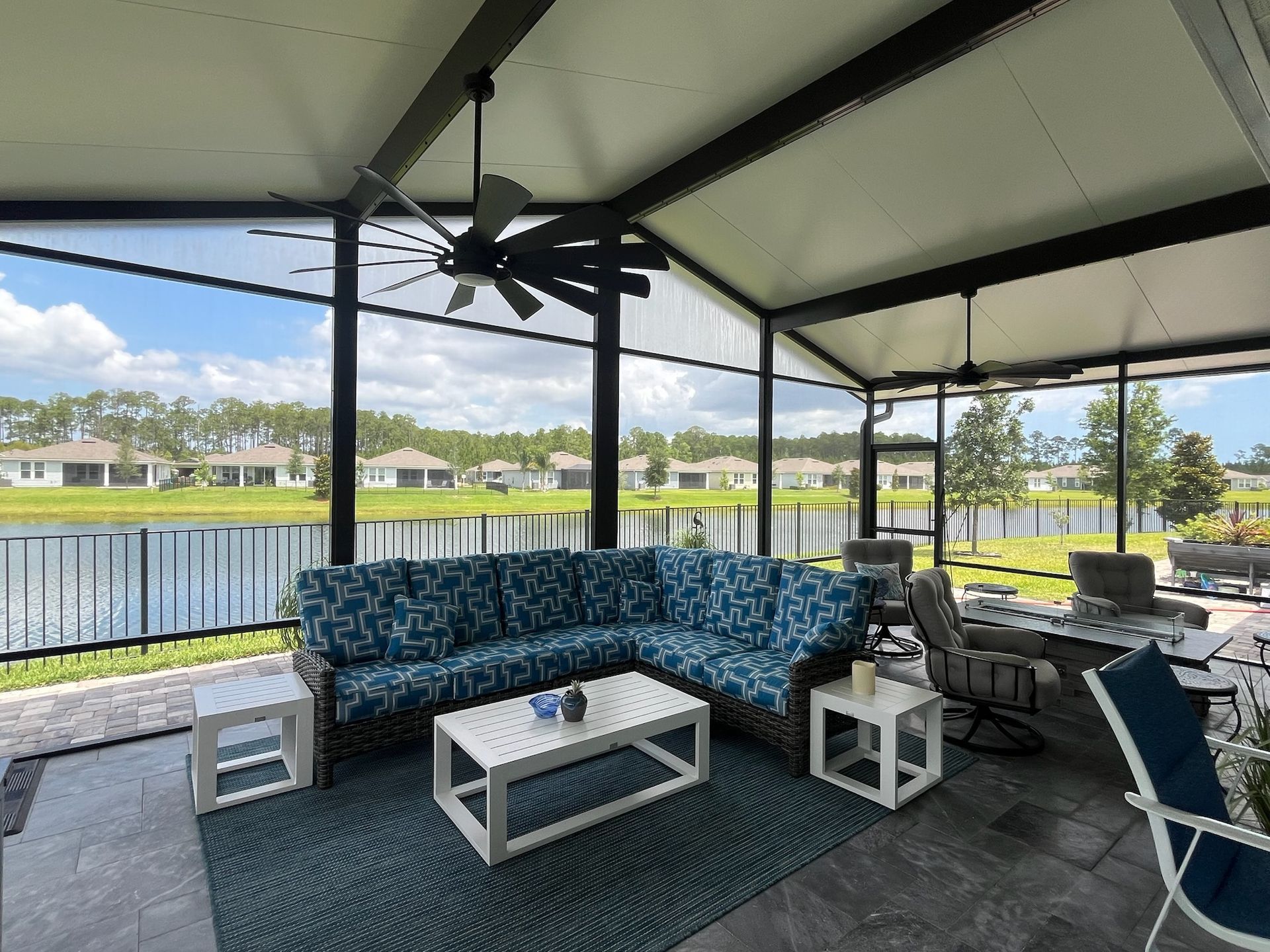 Covered outdoor patio overlooking a lake, with sectional sofa, coffee table, and ceiling fan.