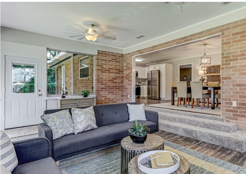Living room with gray sofa, brick walls, and open doorway to dining area.