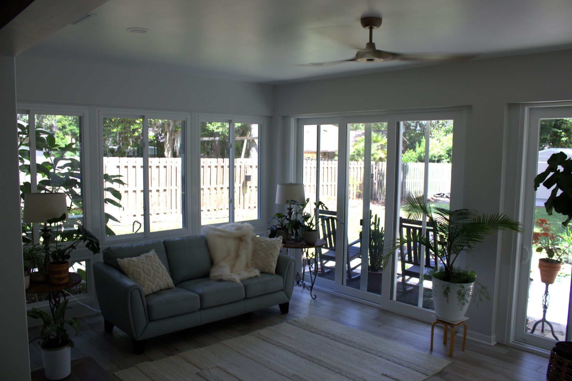 Sunroom with blue sofa, plants, and large windows overlooking a backyard.