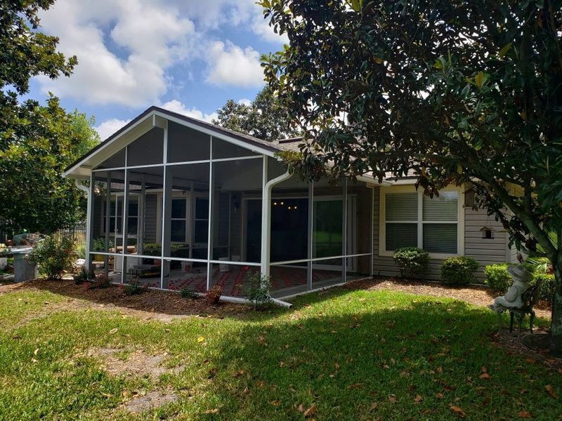 Screened porch with white trim, attached to a light-colored house, under a sunny sky.