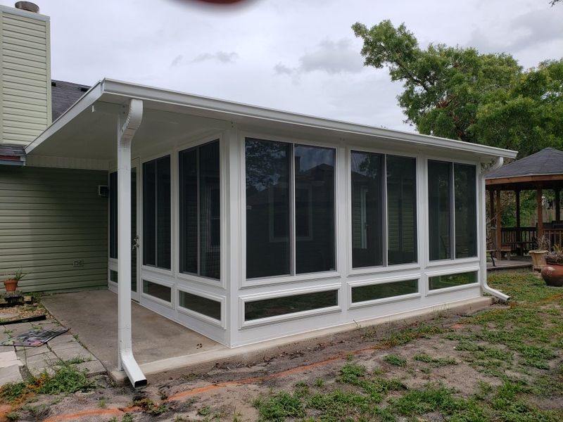 White screened-in porch with windows and a white roof, attached to a light green house.