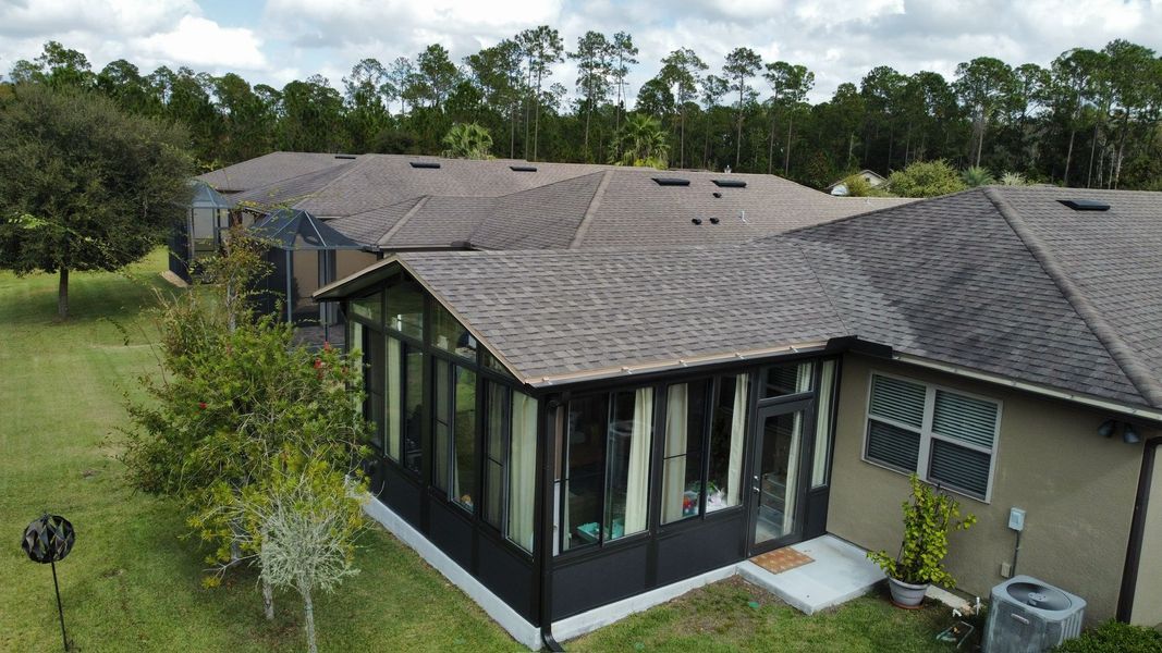 Houses with brown roofs and a screened-in porch, surrounded by green grass and trees.