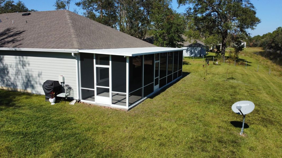 A screen-enclosed patio attached to a house with a brown roof, on a grassy lawn with a satellite dish.