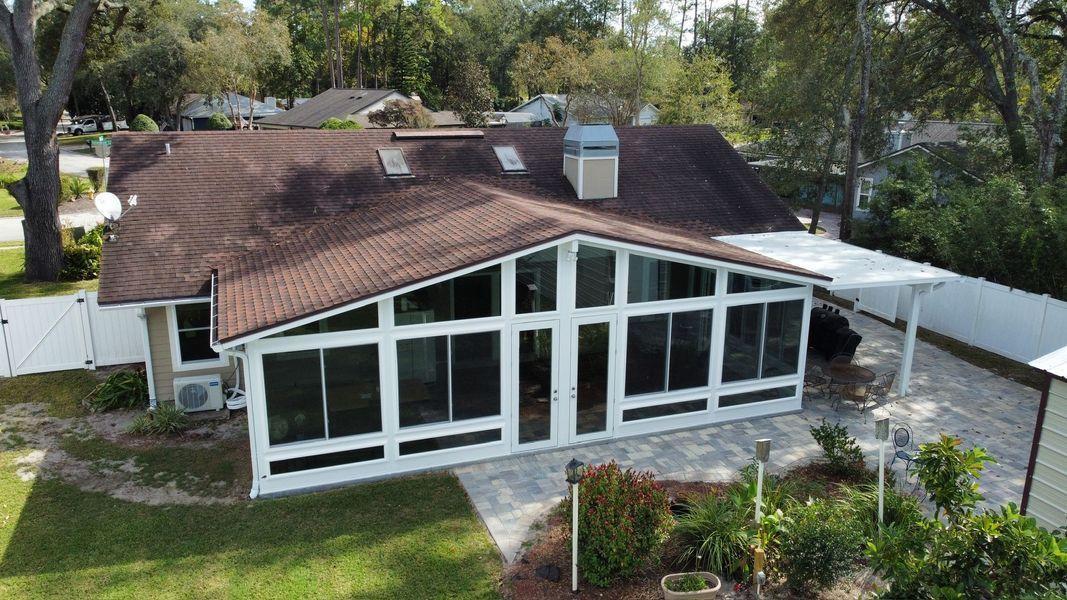 Aerial view of a house with a brown roof and a white screened-in porch with a pergola.