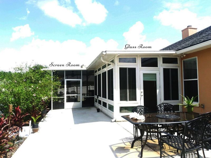 White glass room and screened porch attached to a peach-colored house with a patio and outdoor furniture.