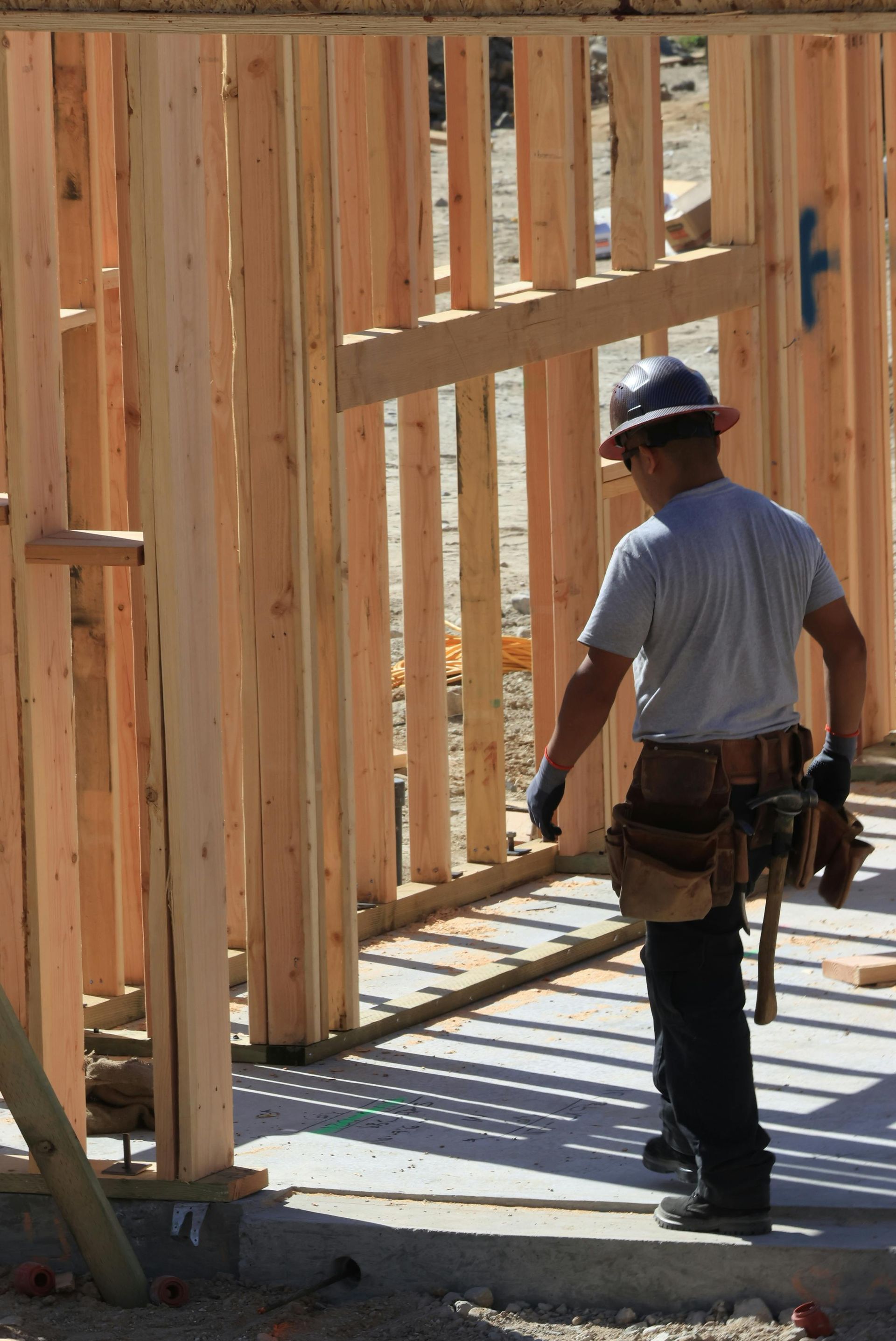 Construction worker stands in a framed wooden building under construction.