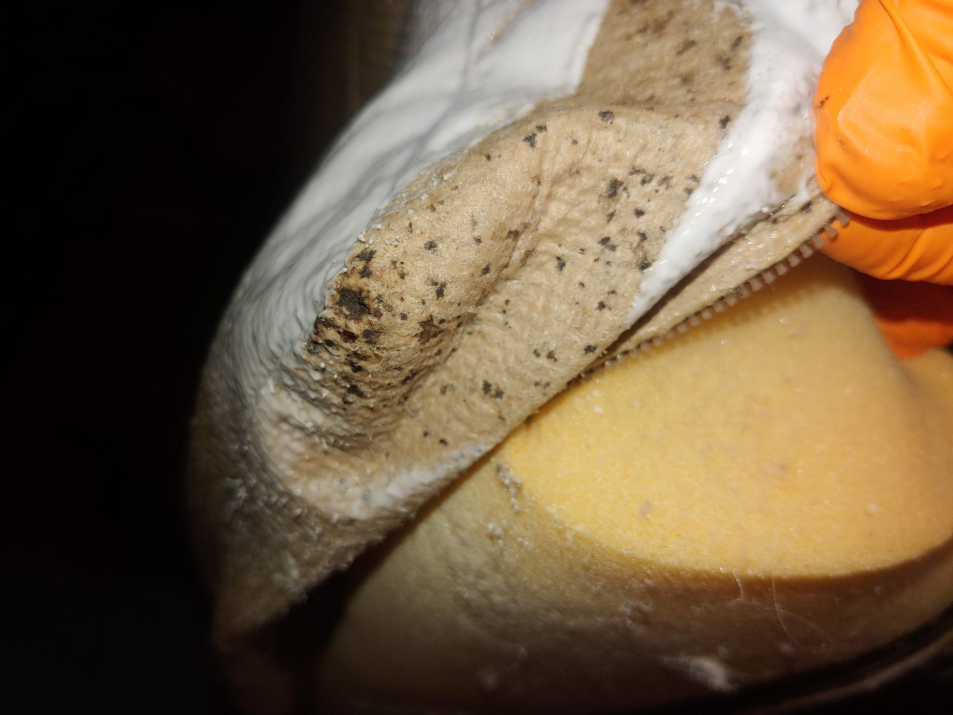 Gloved hand holding a dirty cloth over a yellow object, cleaning or wiping its surface