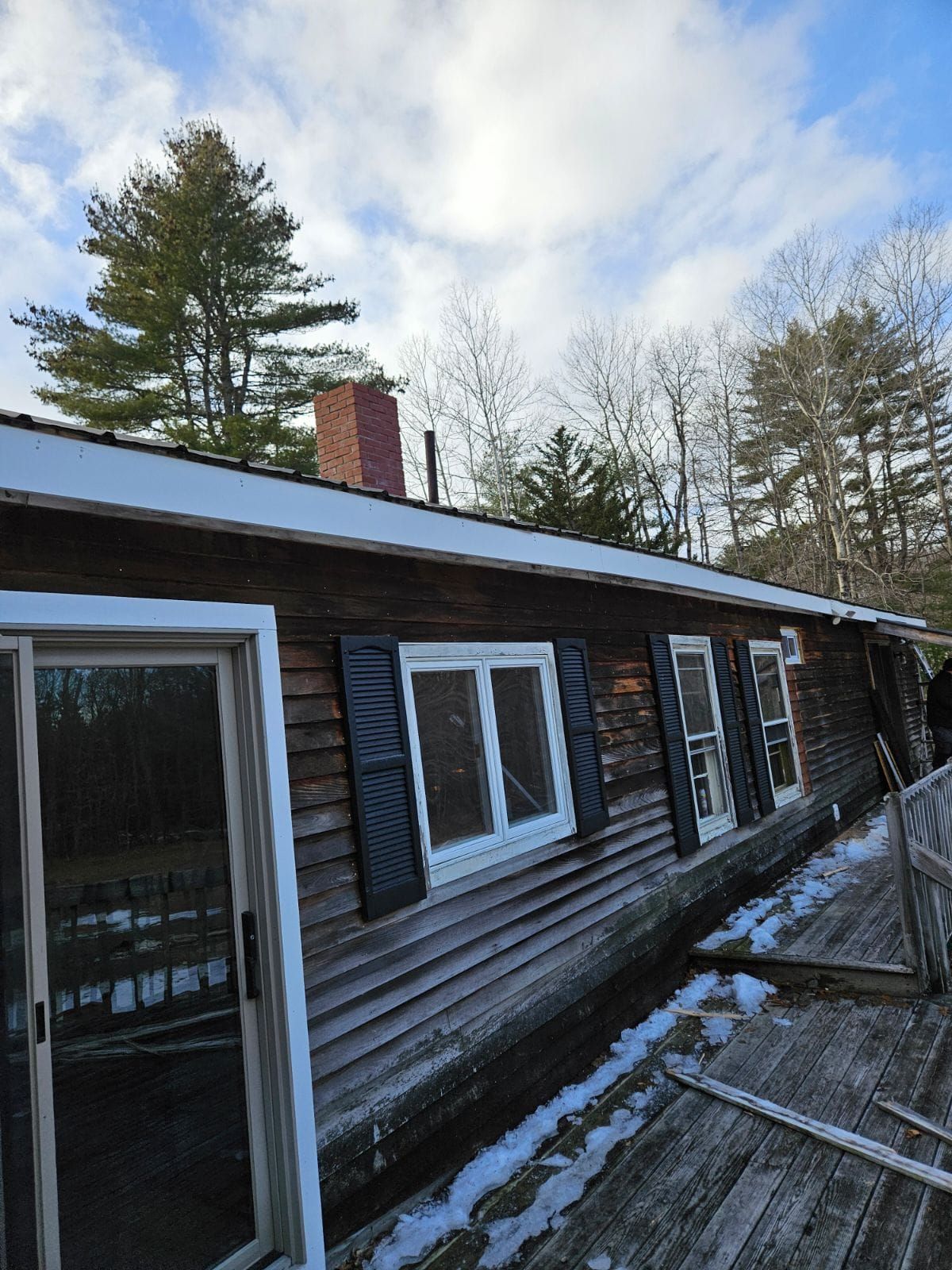 Wooden cabin exterior with windows and a snowy deck under cloudy sky