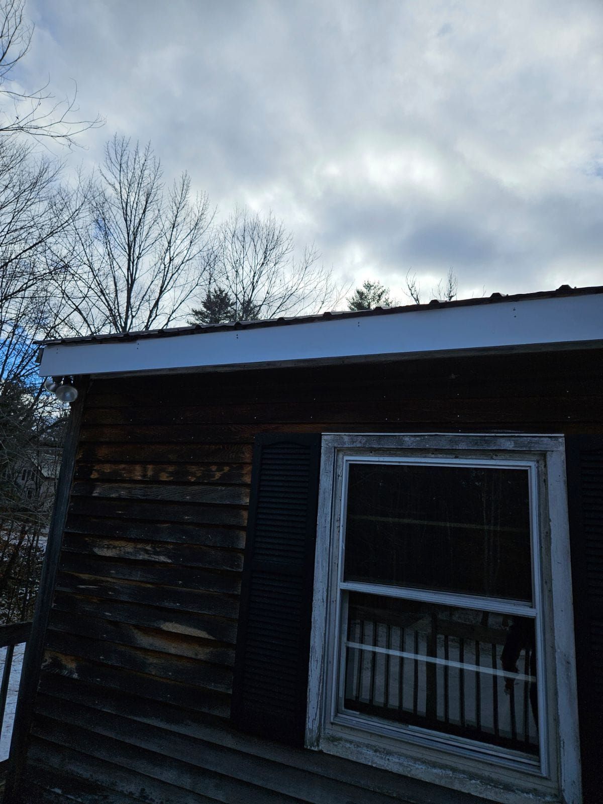 Old weathered wooden shed with a snow-covered roof and a window, under a cloudy winter sky