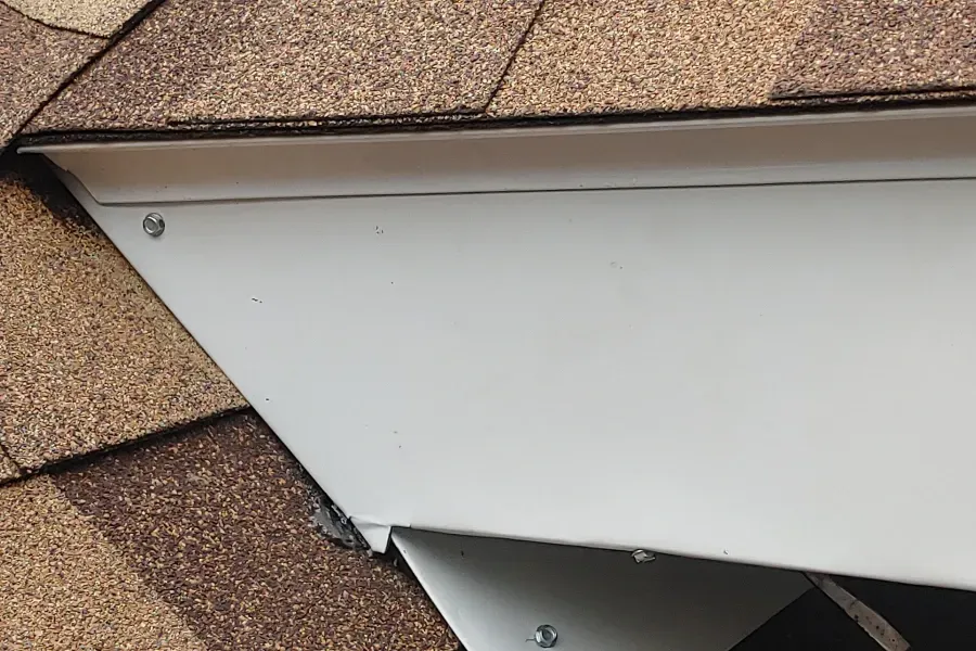 Loose white soffit panel beneath brown shingle roof, partially detached at the eaves.