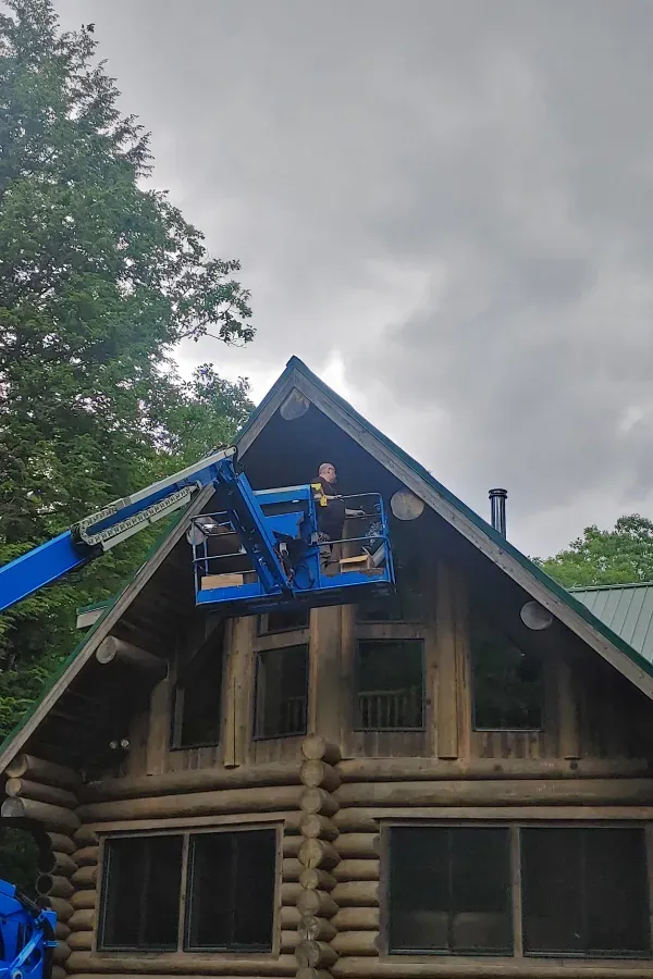 Blue lift with workers repairing the roof of a rustic wooden house under a cloudy sky
