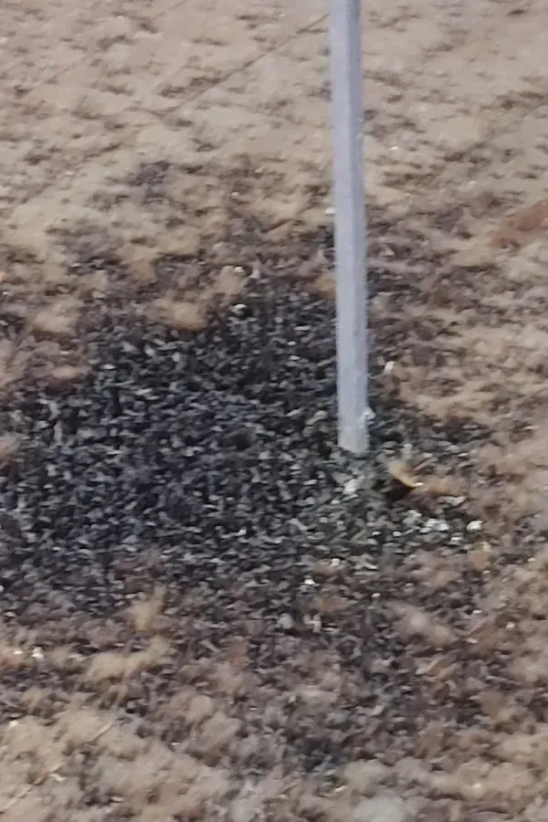 White pole in sandy ground beside a dark patch of spilled material
