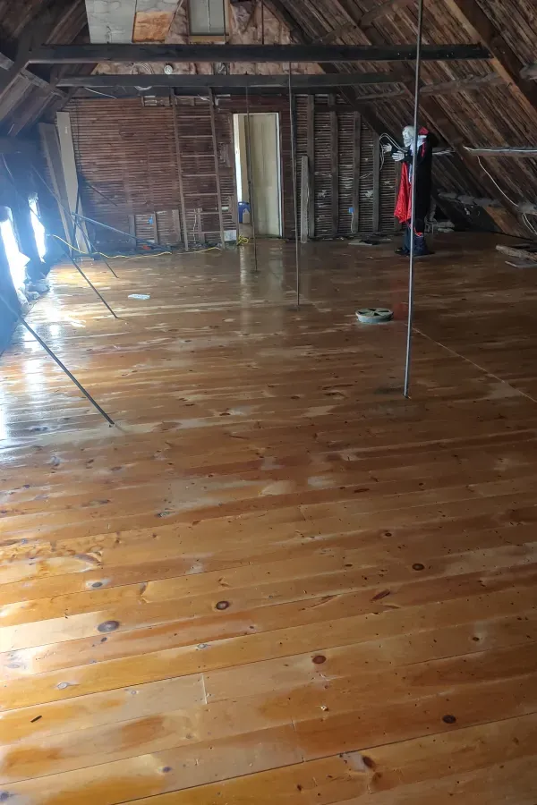 Empty attic with polished wooden floor, exposed beams, and a ladder leaning against the wall.