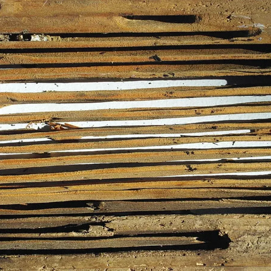 Rusty metal slats with white gaps and black marks, forming a weathered striped surface