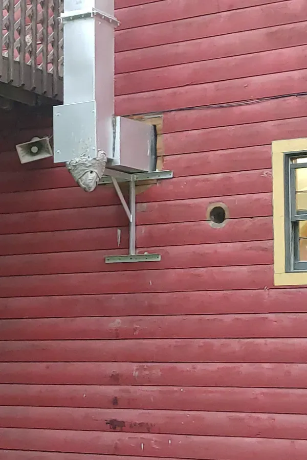 Red wooden exterior wall with a metal vent and support bracket, plus a small window on the right.
