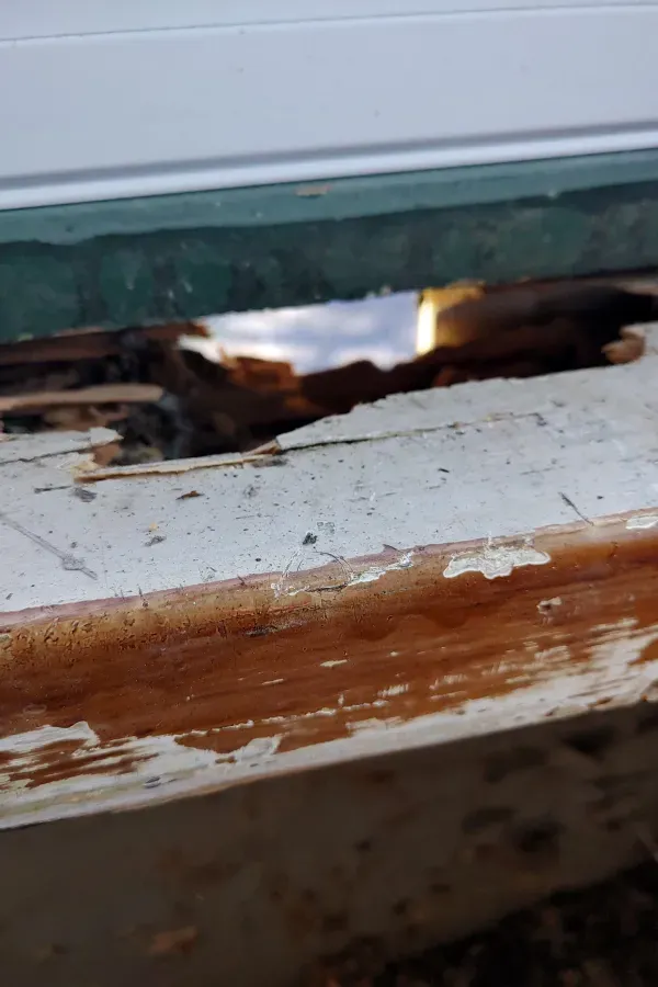 Rotted wooden windowsill with peeling paint and a damaged gap near the frame