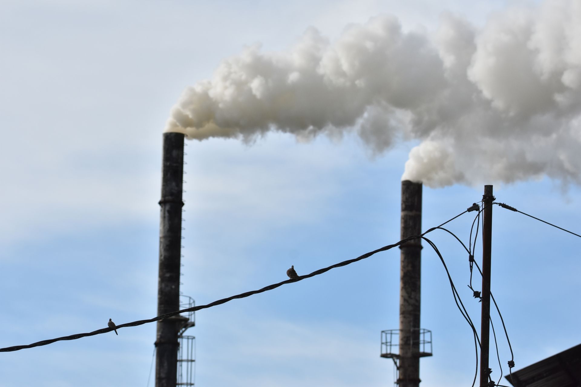 Two chimneys with smoke coming out of them against a blue sky
