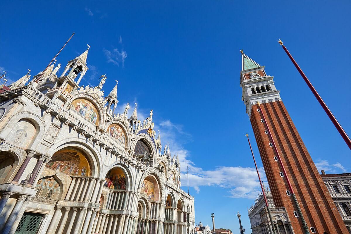 The facade of St. Mark's Basilica and the Campanile in Venice under a clear blue sky.