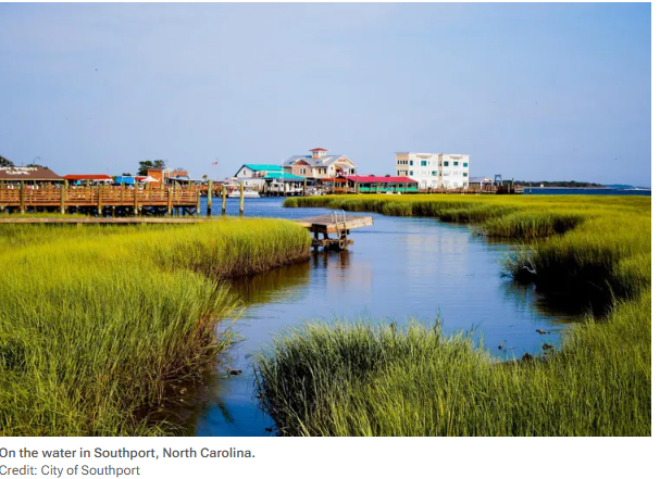 Boardwalk over marsh grass and water in Southport, North Carolina, with waterfront buildings in the distance