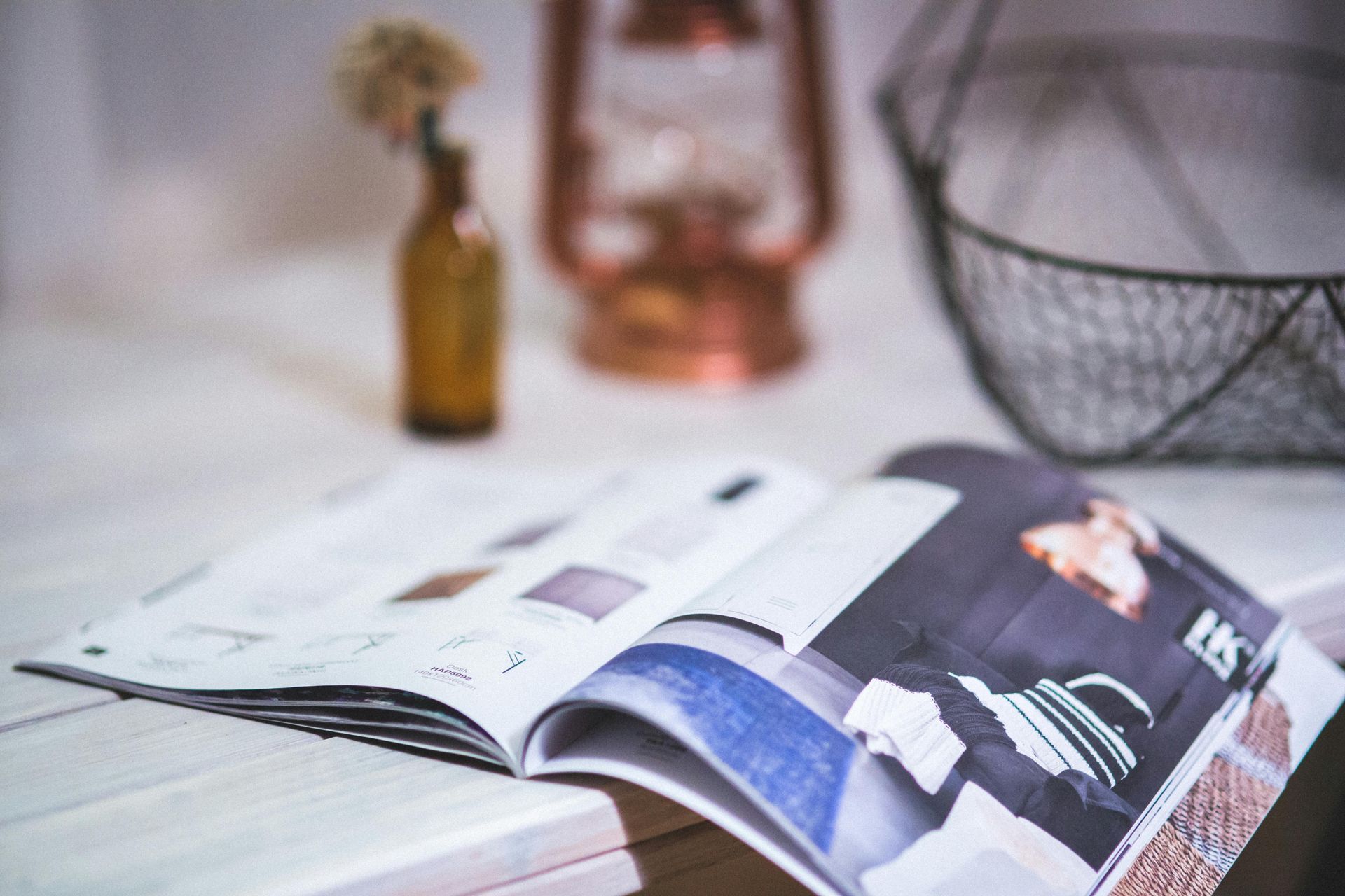 Open magazine on a table with a blurred vase and decorative bowl in the background