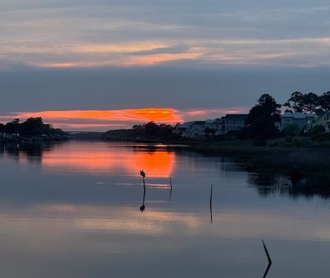 Sunset over a calm river, with orange reflections and silhouetted houses along the far shore