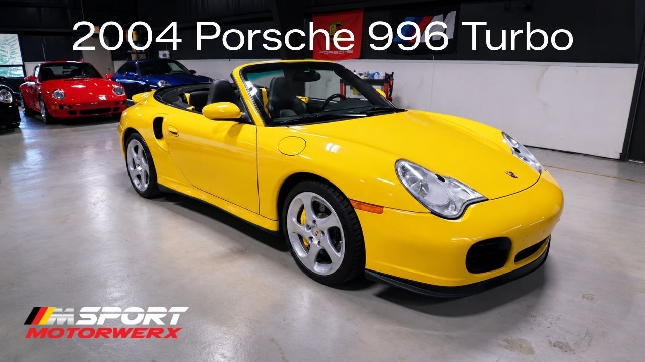 Yellow 2004 Porsche 996 Turbo in a showroom, front-left view, with other cars in the background
