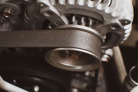 Close-up of a car alternator and pulley with a black belt, part of a vehicle's engine.