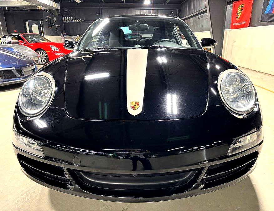 Front view of a black Porsche 911 with a white racing stripe in a garage