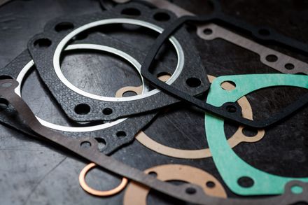 Various black, green, and tan gaskets with holes on a dark surface.
