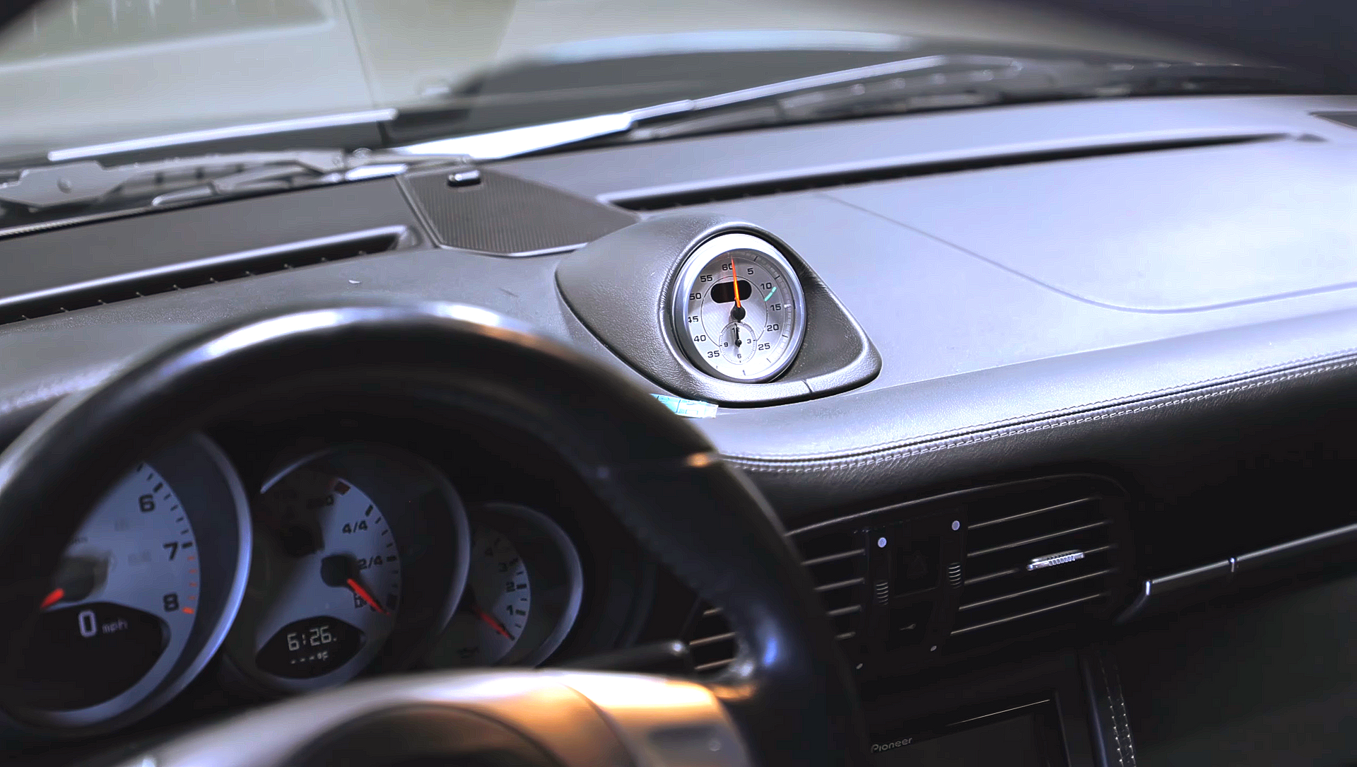 Car dashboard with steering wheel and analog gauges, featuring a small clock on the center console.