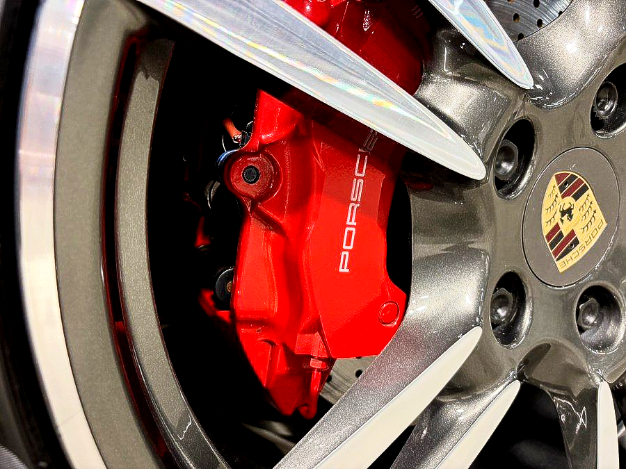 Close-up of a red Porsche brake caliper behind a silver alloy wheel rim